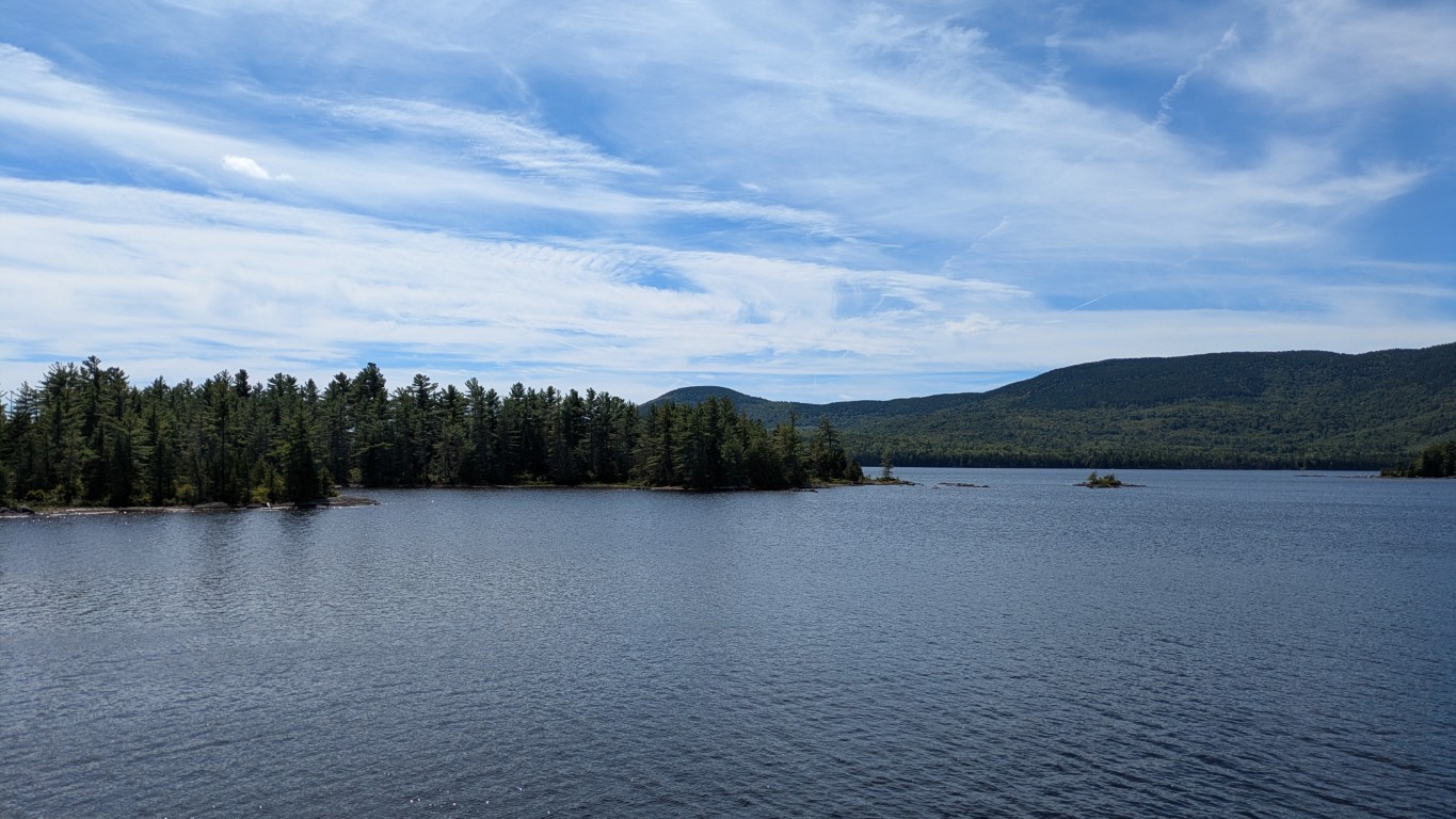 An expansive view of the water, with foreground trees and a forested mountain ridge in the background.