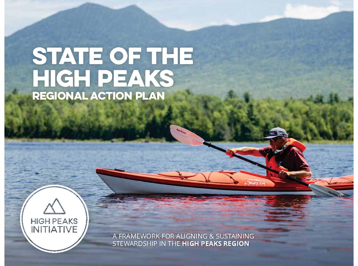 A kayaker on a large lake with a mountain range in the background on a sunny day.